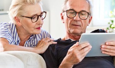 Due anziani seduti sul divano che utilizzano un tablet