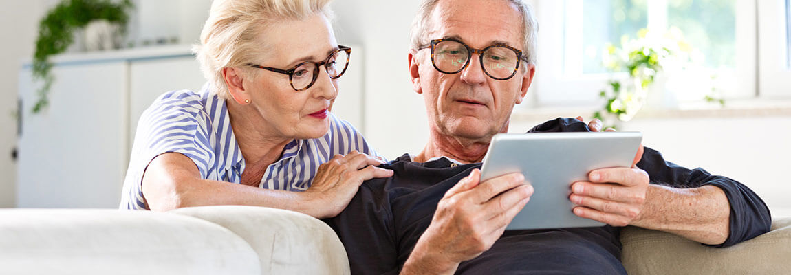 Due anziani seduti sul divano che utilizzano un tablet